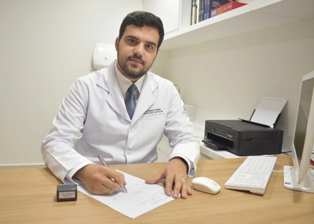Dr. Bruno Cordeiro à mesa do consultório, escrevendo numa folha e olhando para a câmera.