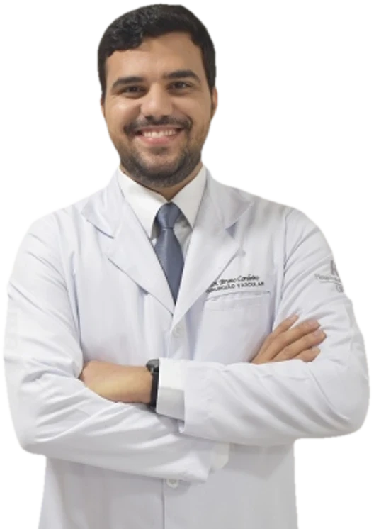 Dr. Bruno Cordeiro em pé, de jaleco branco e gravata azul, braços cruzados, sorrindo.
